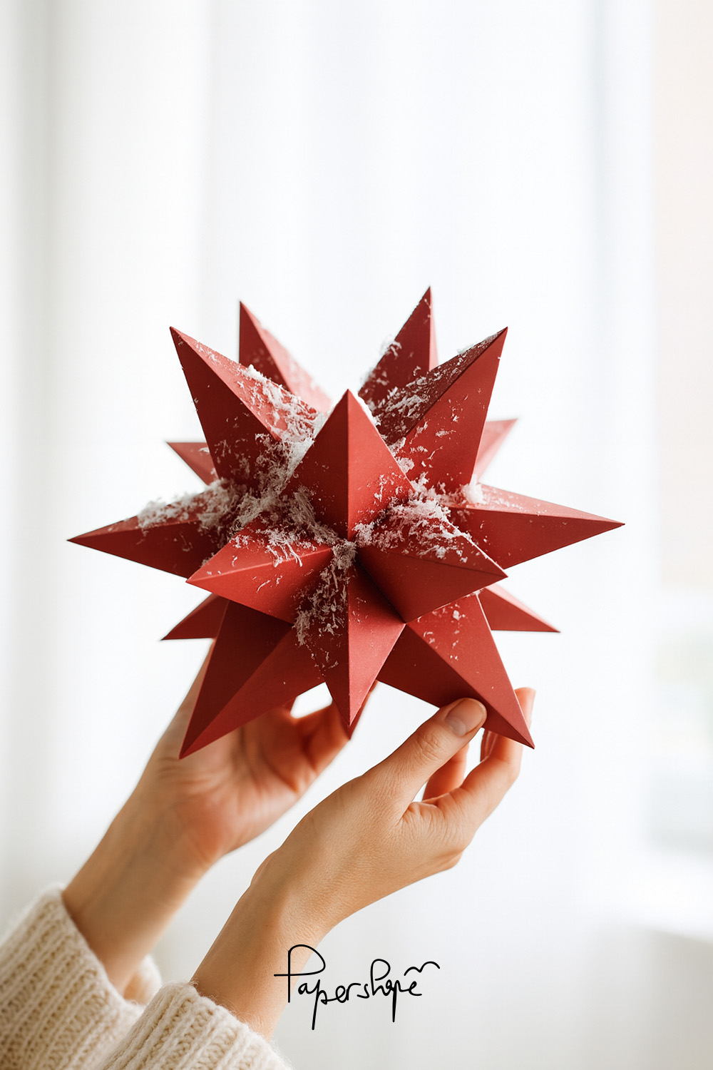 DIY XXL Christmas star: Red geometric paper star with snowflakes, held by female hands in soft natural light
