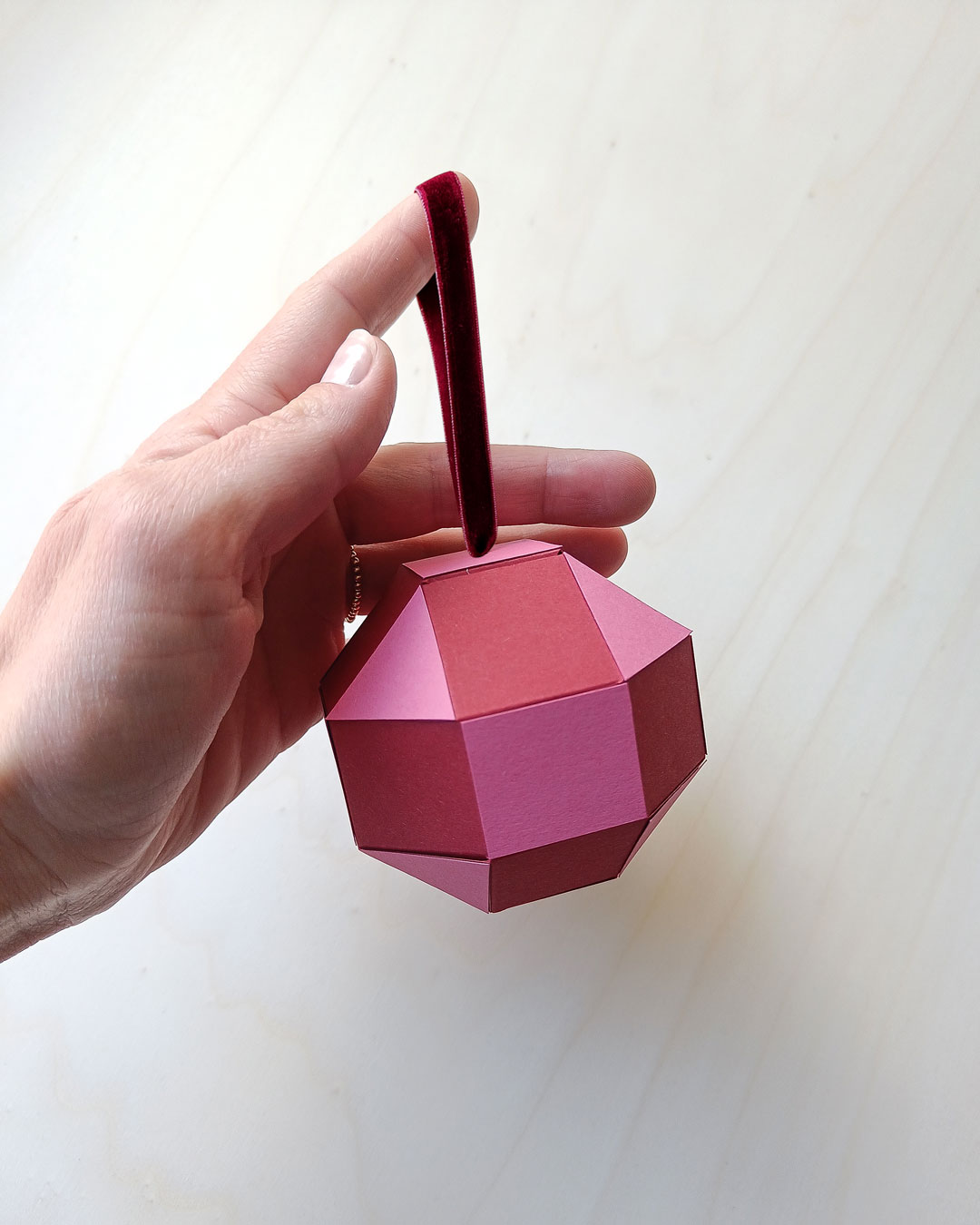 Hand hält ein rotes geometrisches Papierornament mit Samtband - moderne Weihnachtsdekoration.