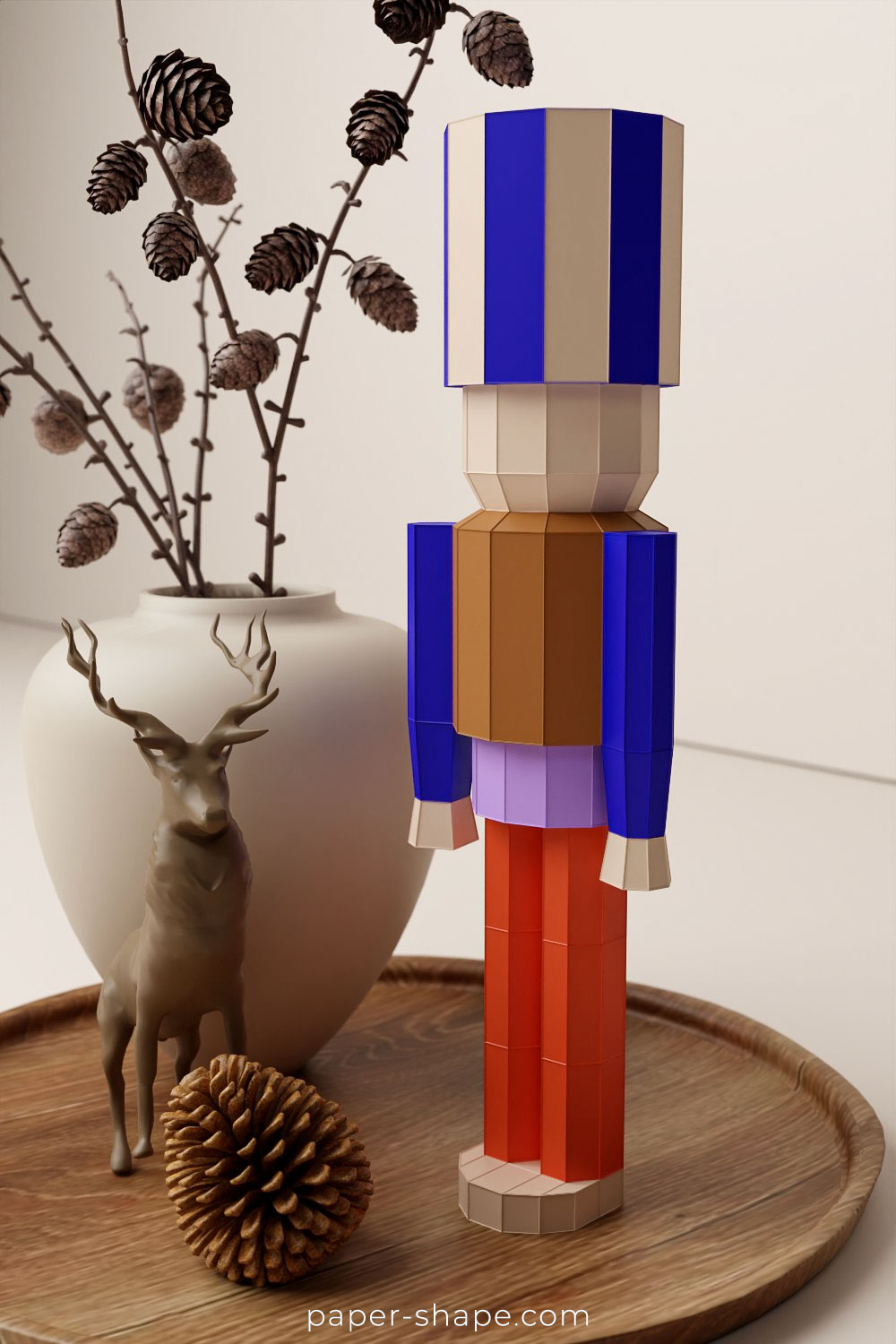 Colorful paper nutcracker next to a vase, an elk sculpture and pine cones against a beige background