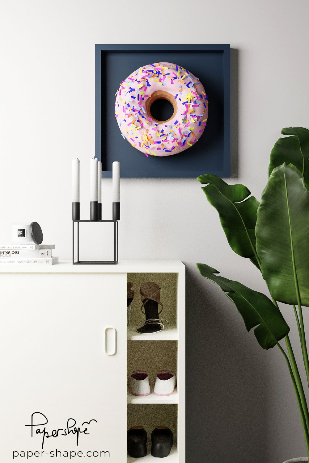 Papercraft Papier-Donut in einem anthrazitfarbenen Rahmen als moderner Farbakzent auf weißem Sideboard.
